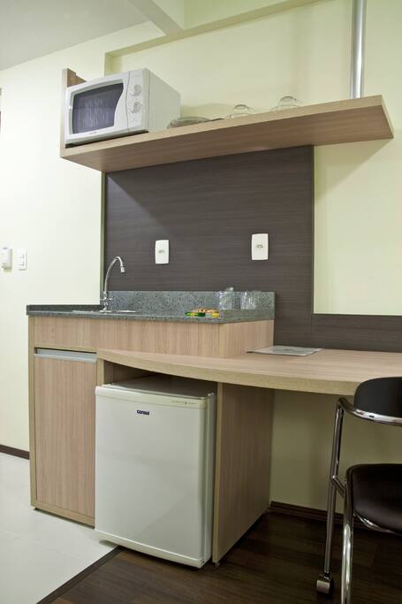 Cozinha compacta com microondas, frigobar, pia, copos, talheres e pratos.