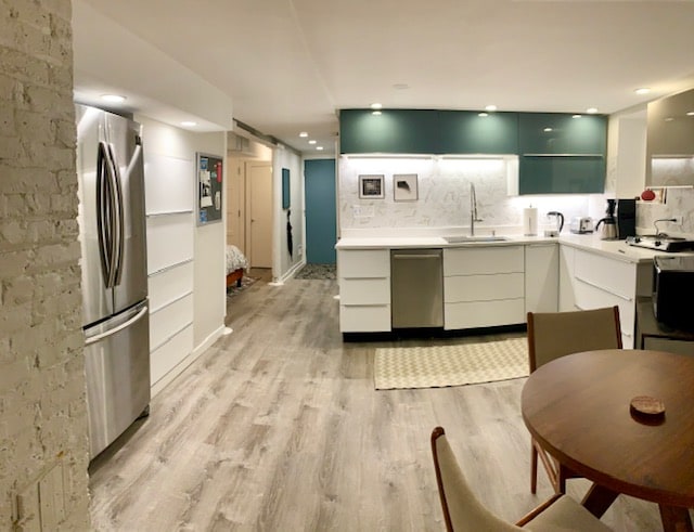 A modern kitchen is visually prominent, featuring sleek cabinetry and stainless steel appliances. A small mid-century dining table with matching chairs is situated in the foreground. Warm light illuminates the space, highlighting the neutral tones of the walls and wood-style flooring.