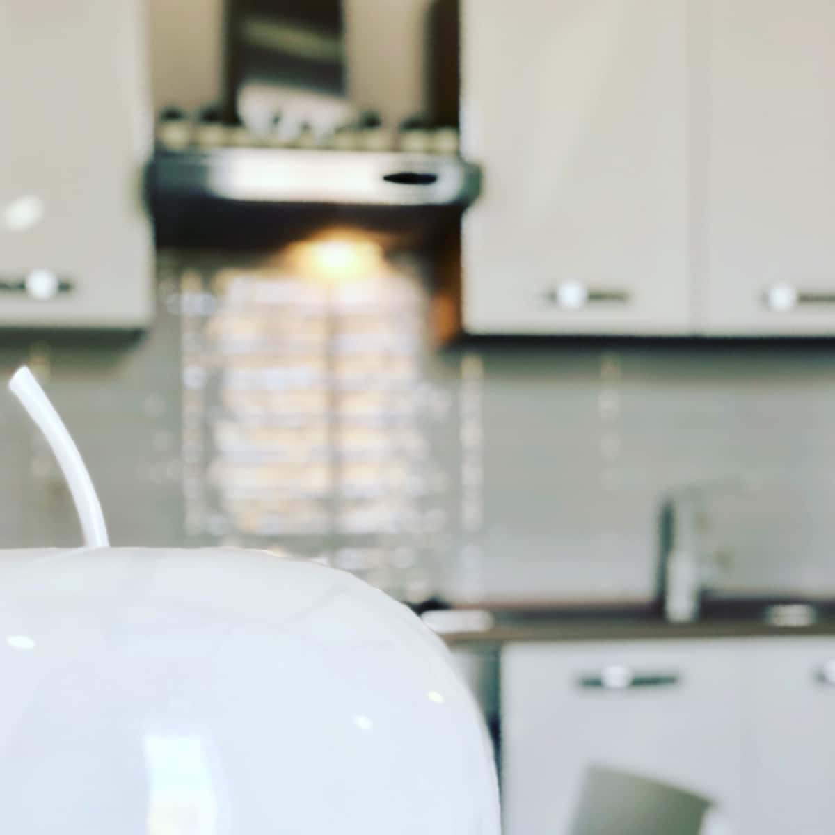 A modern kitchen space is depicted, featuring sleek cabinetry and a stainless steel hood above the stove. The foreground highlights a white decorative item, creating a contemporary aesthetic. Soft lighting from the countertop provides a warm ambiance, enhancing the functional design of the kitchen area.