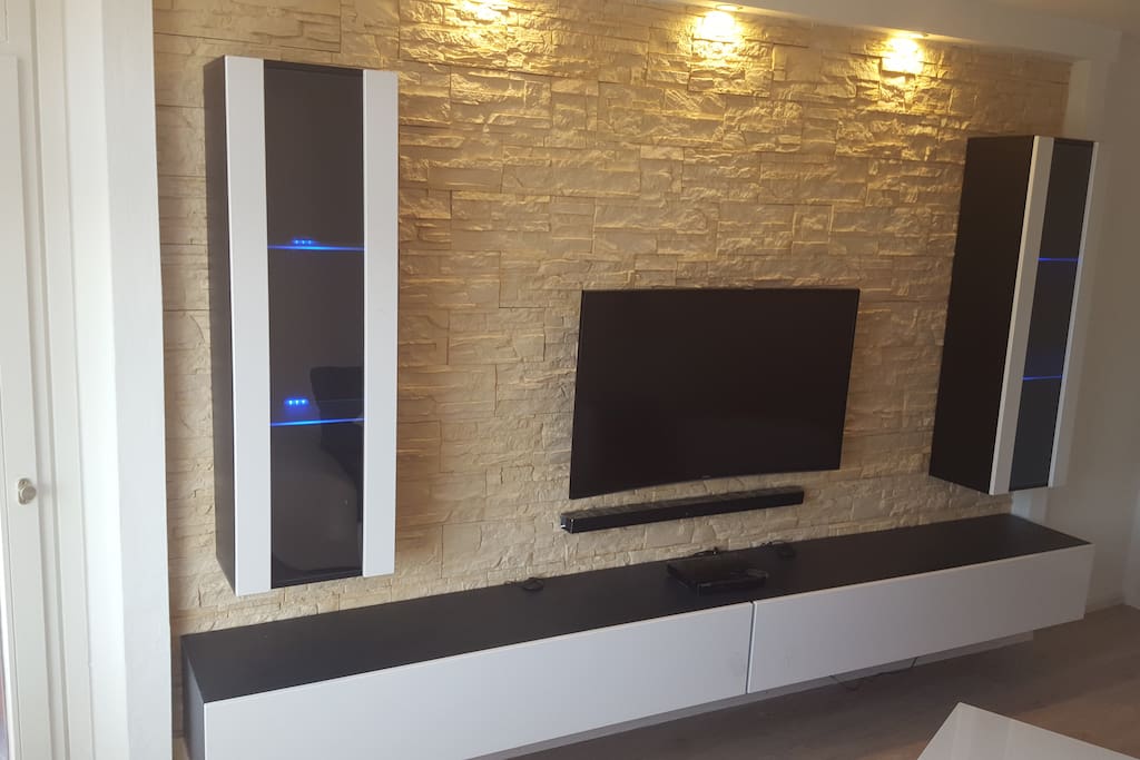 Im Wohnzimmer genießen sie auf einen 48 Zoll großen Curved TV Inhalte in bestechend scharfer UHD Qualität (Samsung UHD-Erlebnispaket). Über eine kabellos angeschlossene Soundbar haben sie den passenden, hochwertigen Sound dazu. Zudem sind über eine zentrale SAT-Anlage deutsche und einige ausländische Kanäle empfang bar. Ein Blu-ray Player gehört selbstverständlich ebenfalls zum Inventar.