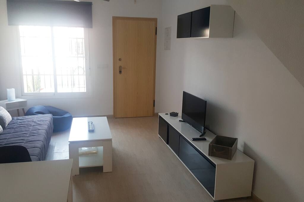 Salón de la casa con televisión, mesa para comer, sofá cama y sillón