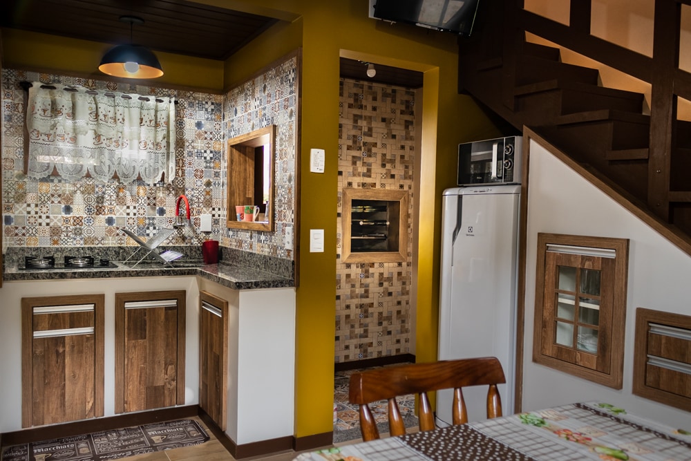 A modern kitchen area features an array of patterned tiles and granite countertops. Wooden cabinets are complemented by a refrigerator and built-in oven. A dining table with wooden chairs is visible, creating a functional space for meals. Decorative elements accentuate the design.