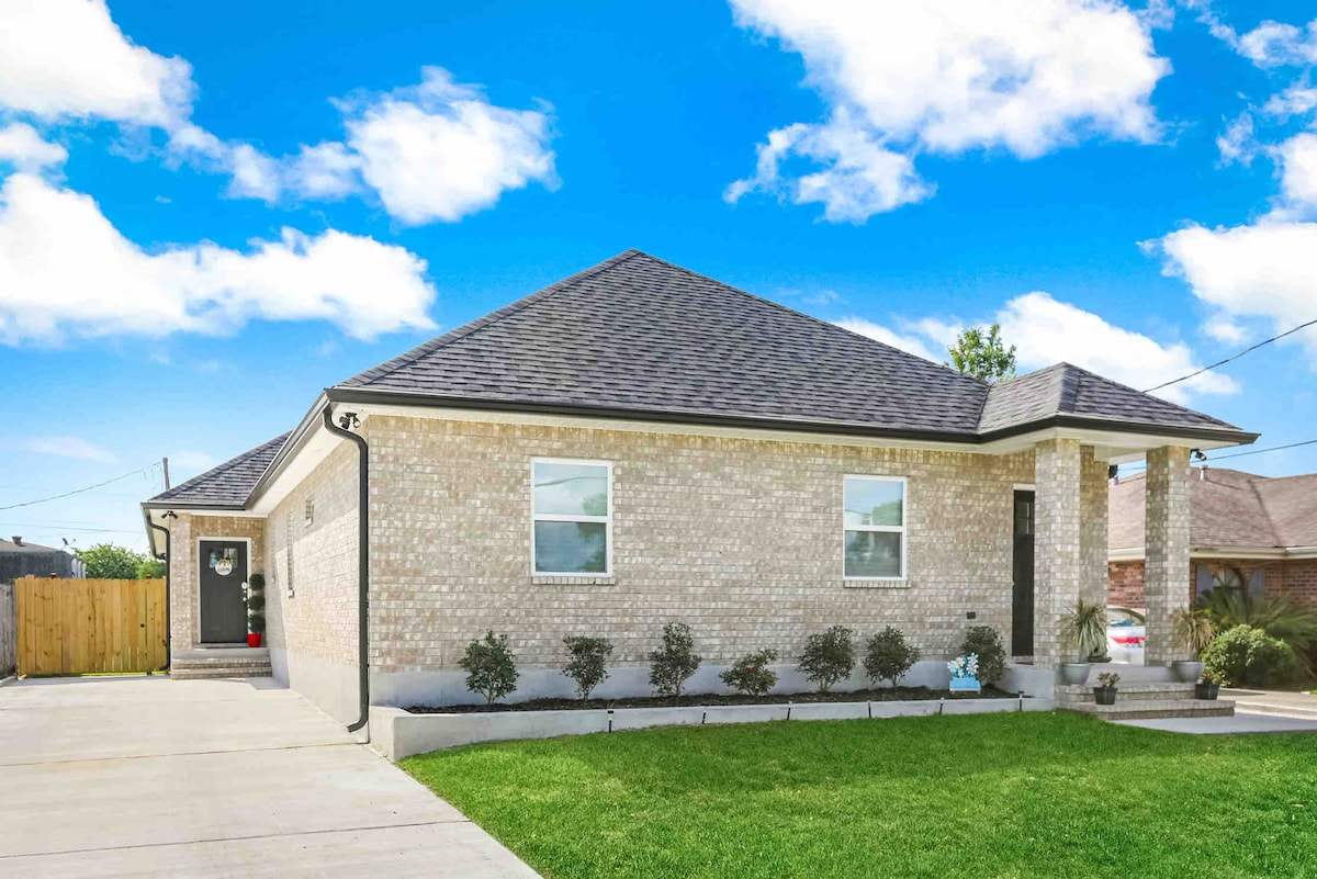A newly constructed double house is presented, featuring a light brick exterior and a well-maintained front yard. Two large windows allow natural light to illuminate the space, and a driveway leads to the entrance. The surrounding greenery enhances the home's curb appeal.