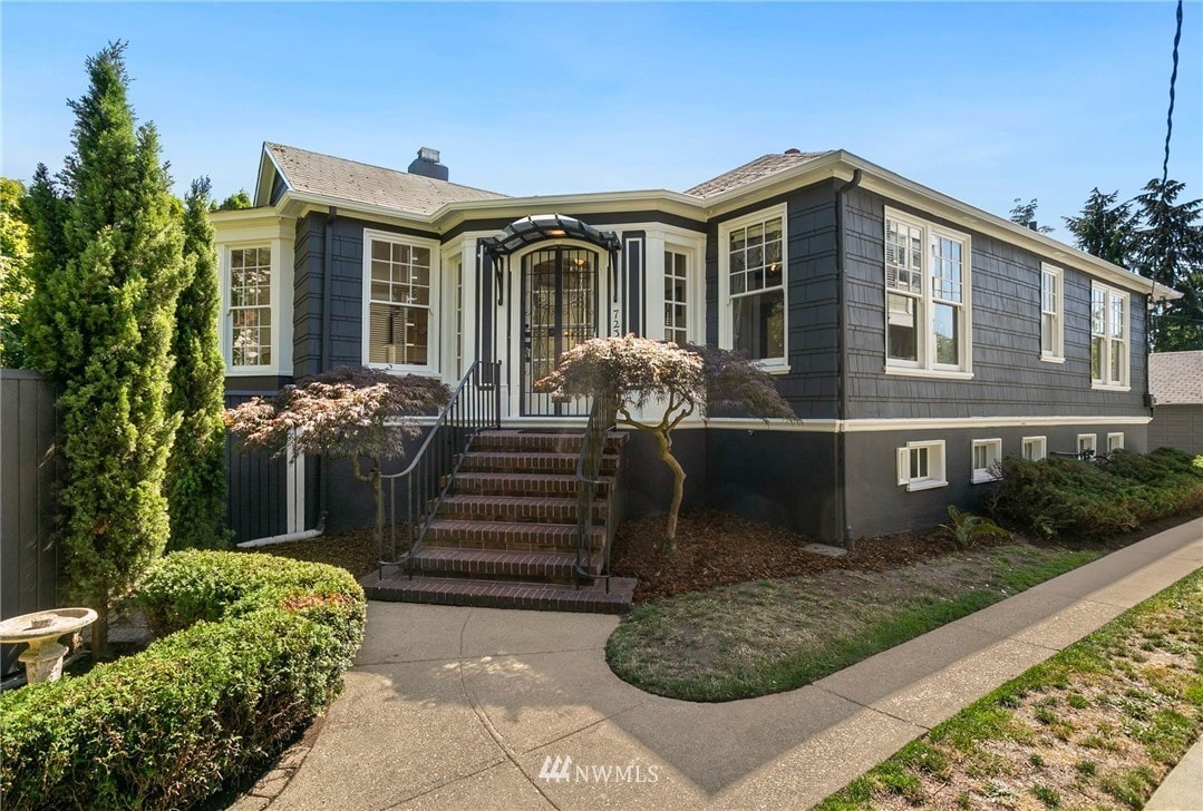 The exterior of a distinguished two-story home is presented, featuring dark siding and large windows. A landscaped yard with neatly trimmed hedges lines the walkway, which leads to a distinct archway entrance. The overall aesthetic blends historic charm with modern appeal.