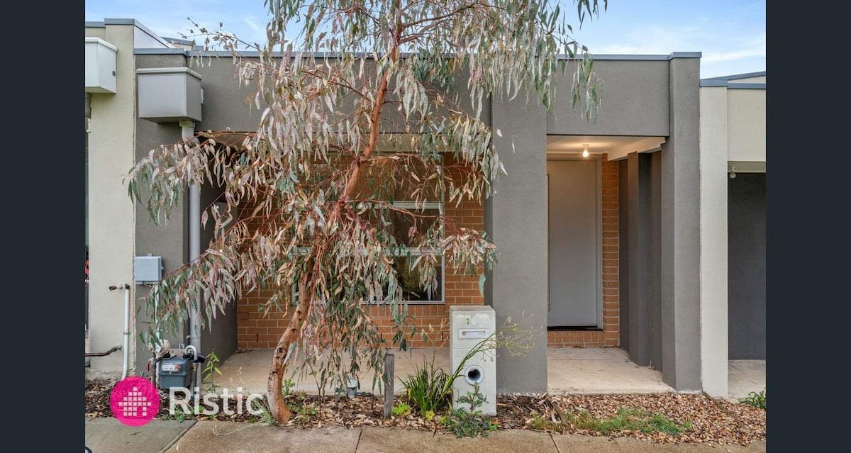 The exterior of the unit features a combination of brick and smooth gray walls. A native tree is visible in front, complemented by gravel landscaping. The entrance is welcoming, with a covered area that leads to the door. The setting maintains a clean and modern appearance.