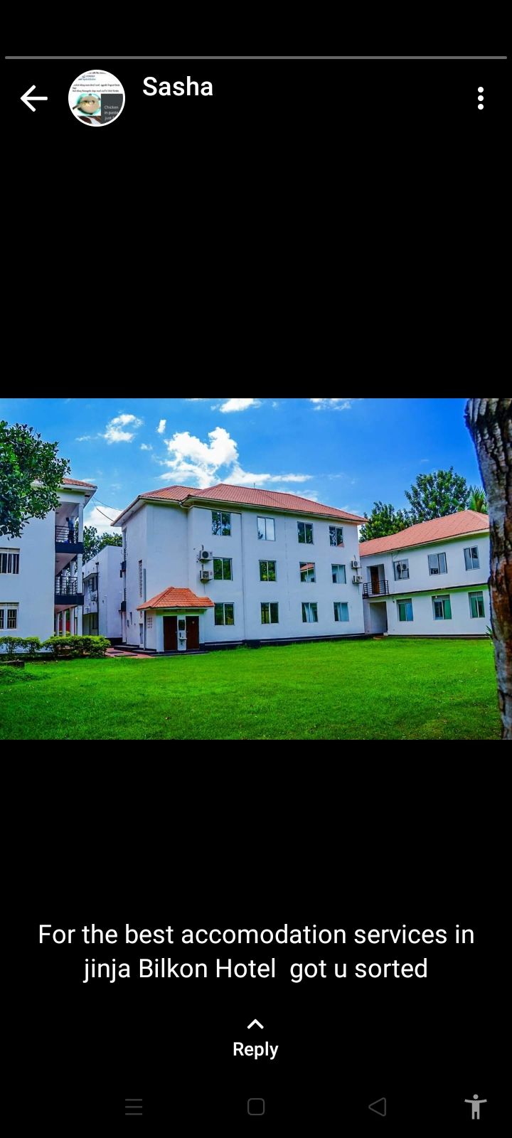 A modern three-story building with a white façade and terracotta roof is surrounded by a well-maintained green lawn. Large windows reflect the blue sky and fluffy clouds, enhancing the spacious feel of the property.