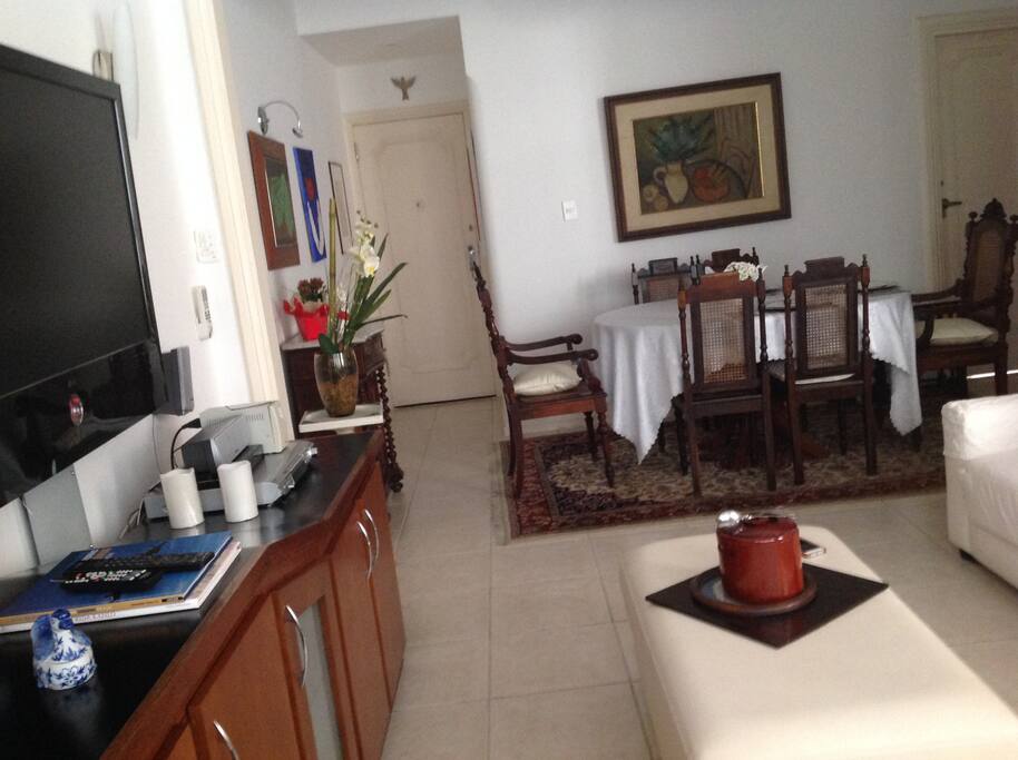 Ampla sala com 3 ambientes: sala de jantar, sala de estar com TV, e estudio.