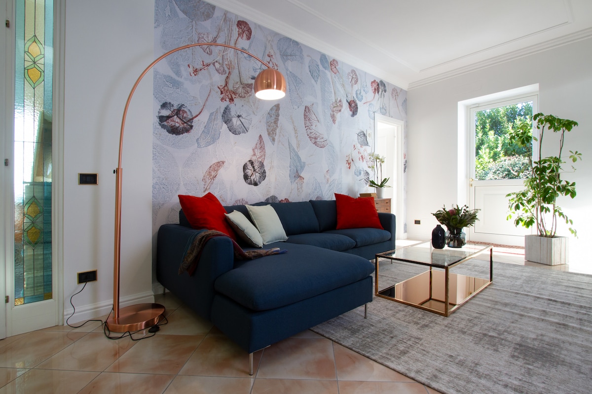 A modern living area is highlighted by a dark blue sectional sofa adorned with red and cream cushions. A sleek glass coffee table rests on a light-colored rug, while a decorative plant adds a touch of greenery. Natural light streams through the nearby window.