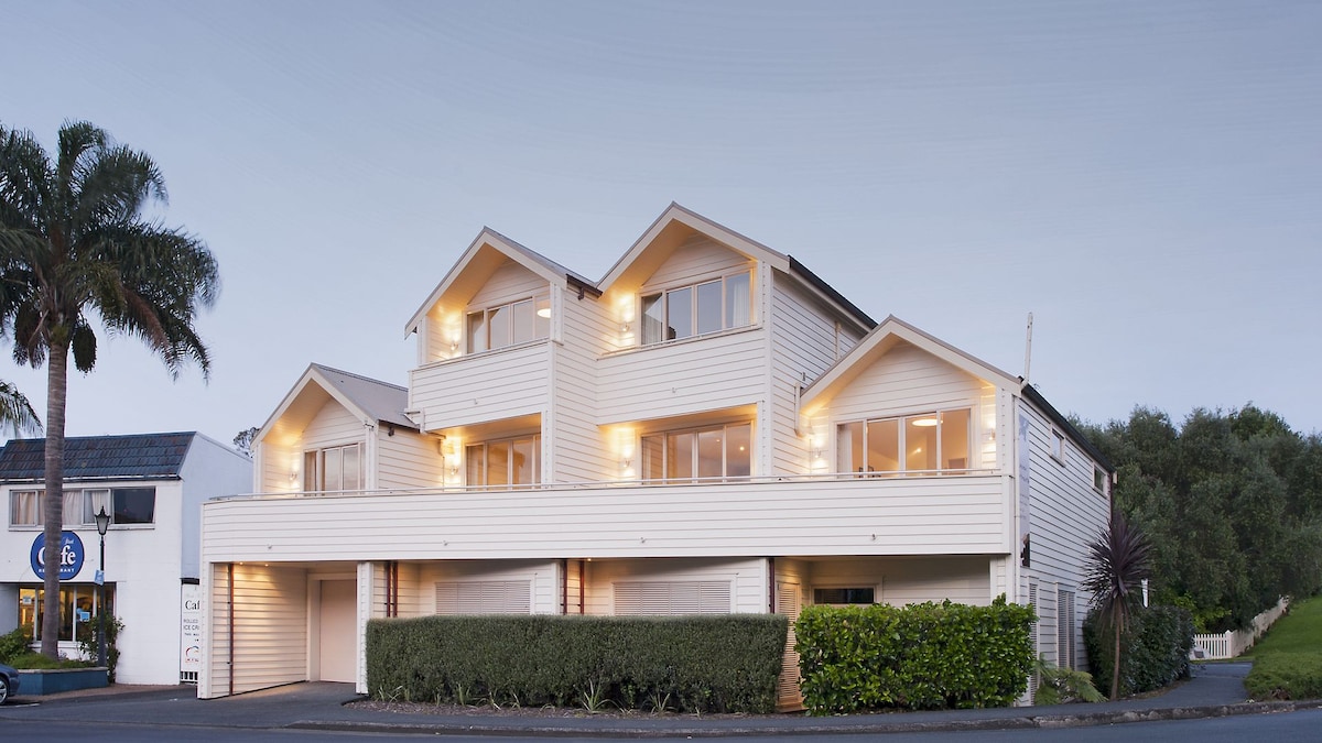 The exterior of the building features a modern design with three peaked roofs and large windows that provide ample natural light. Soft outdoor lighting highlights the architectural details. A neatly trimmed hedge lines the front, adding to the inviting appearance of the property.