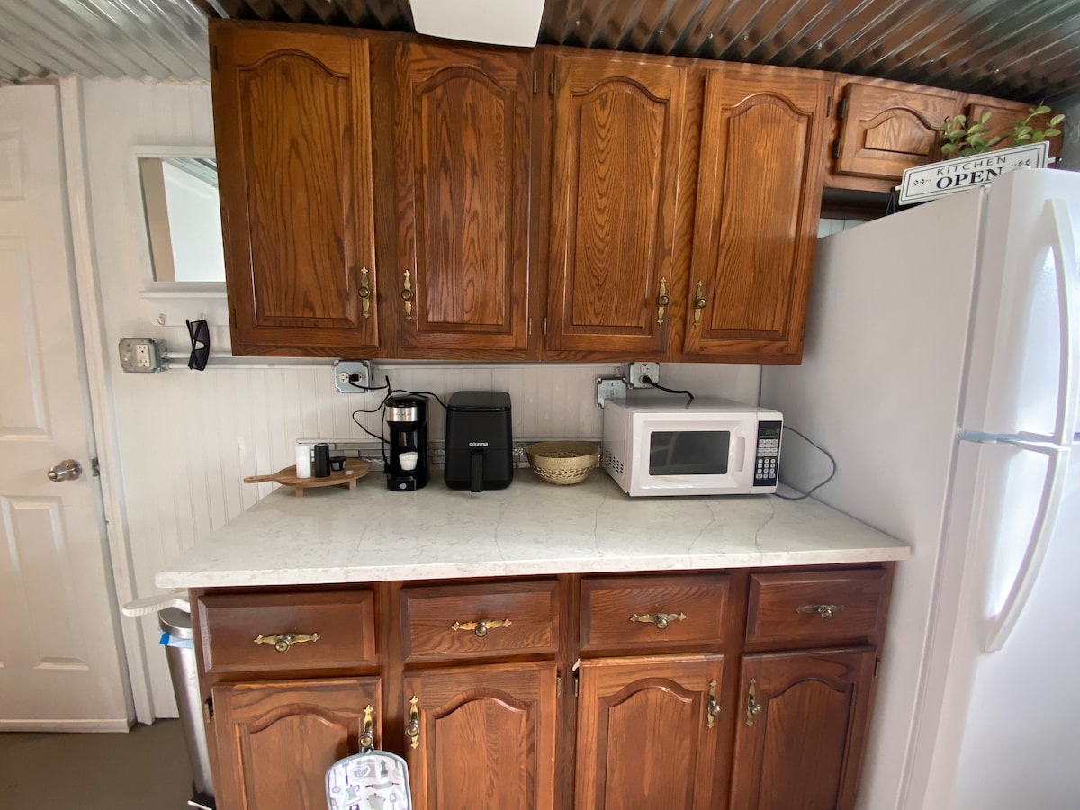 A well-equipped kitchen area features wooden cabinets, a countertop with an electric coffee maker, and a microwave. Nearby, a refrigerator stands against the wall, adding convenience for meal preparation. The space is designed for functionality, creating an inviting environment for cooking.