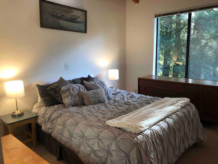 Chambre principale avec grande fenêtre laissant entrer la lumière du jour, tables d'appoint, lampes et commodes pour le rangement des vêtements. 