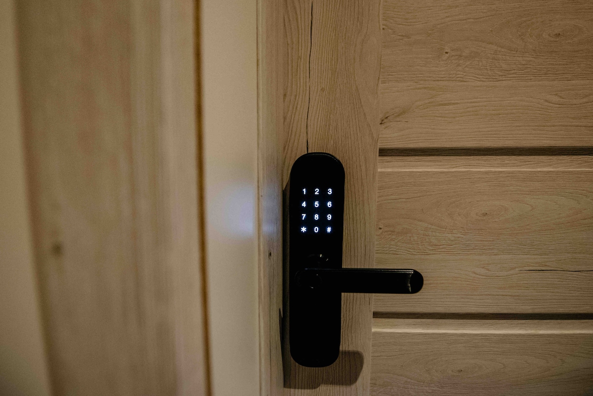 An electronic door lock is displayed on a wooden door, featuring a keypad illuminated with numbers. The smooth wooden texture of the door contrasts with the sleek design of the lock, emphasizing modern security features.