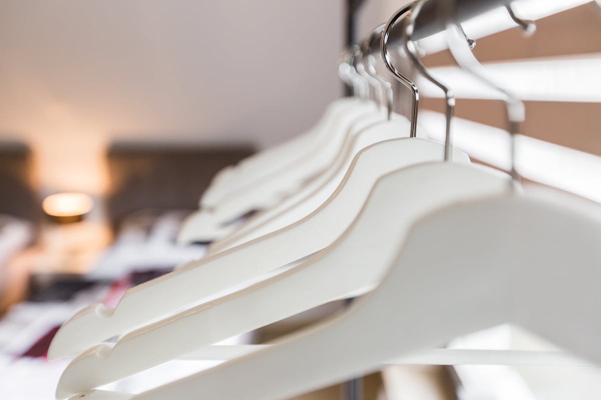 A row of white hangers is displayed on a metal rack, positioned in clear focus. The background reveals blurred outlines of a cozy sleeping area with a soft glow, suggesting a relaxed ambiance.