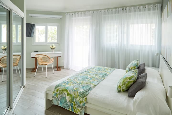 Chambre 2 - lit King Size avec luxueux draps en coton égyptien de couleur vert menthe, télévision intelligente, meuble vasque/bureau avec miroir de meuble vasque et commode