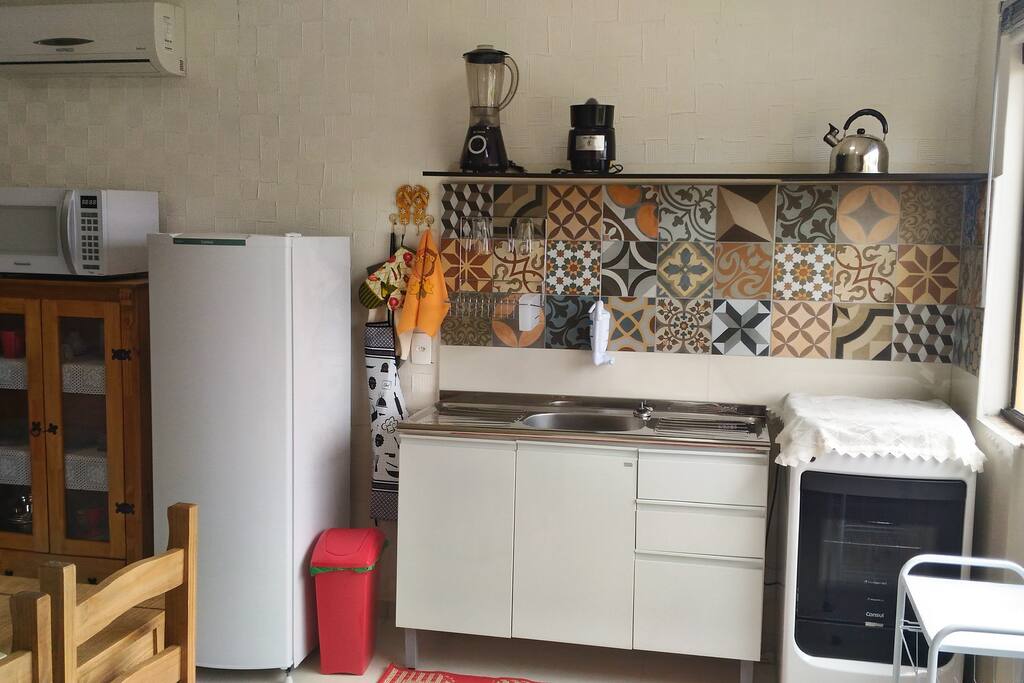 Cozinha com fogão, forno, pia, geladeira, microondas, louças, panelas e utensílios variados.