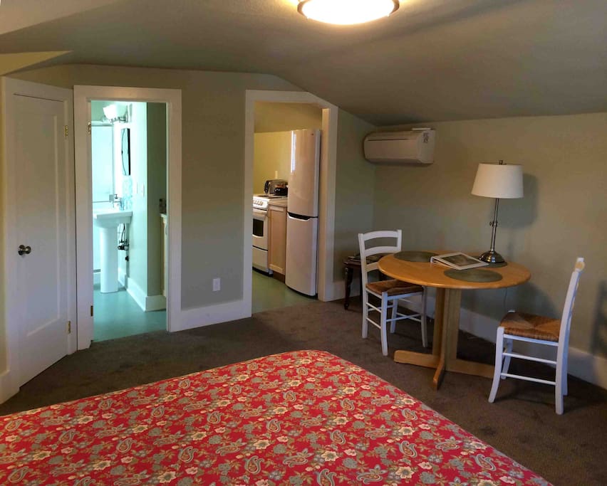 Table and chairs, a flatscreen TV and reading corner, and queen bed in the main room