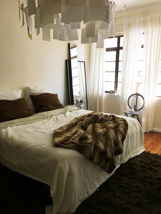 Luxuriously huge bedroom with chic linen sheets and king size bed, looking onto treelined street