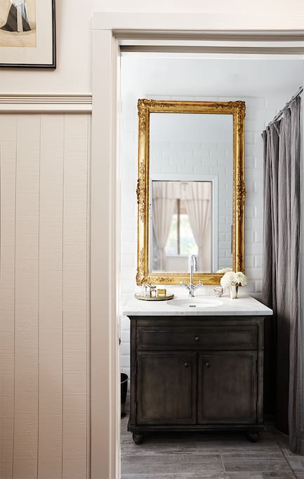 A gorgeous antique french mirror adorns is the center piece of the fully modern bathroom with a rustic feel.