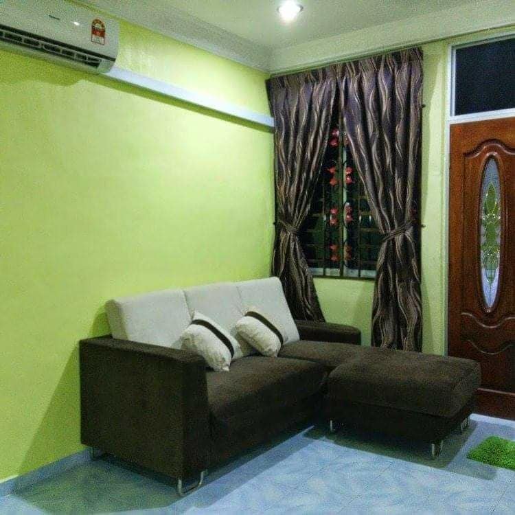 A comfortable seating area is featured with a dark brown sofa that includes decorative pillows. Light green walls provide a fresh backdrop, while patterned curtains frame a window, allowing natural light to illuminate the space.