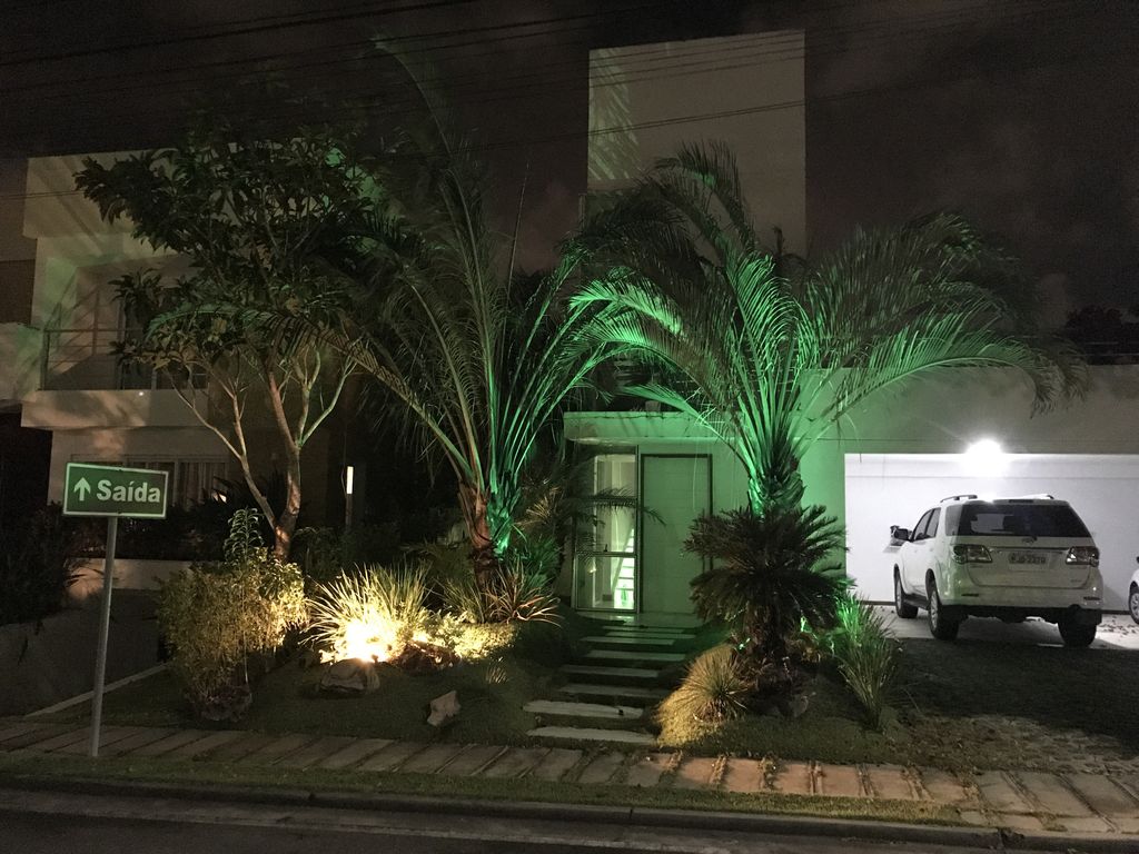 The exterior of the property is shown at night, featuring well-lit palm trees and garden areas. A white vehicle is parked in the driveway, and an illuminated pathway leads to the front entrance. A sign indicating 'Saida' is visible, guiding visitors.