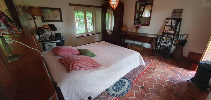 Vue de la chambre prise de la kitchenette,avec son lit Queen size( 160cm ×2m)et une de ses 2 fenêtres donnant sur le jardin. 
Elle comporte également du mobilier ancien rustique chiné, armoire,2chaises basses,
pétrin, poêles, escabeau,porte manteau. 