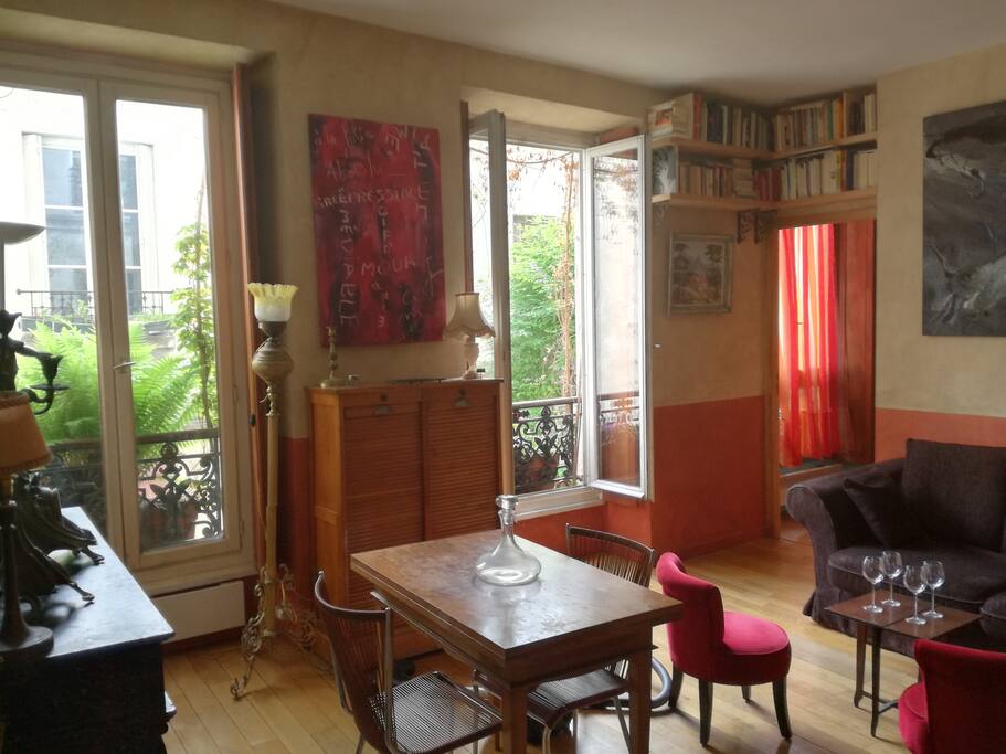 Le séjour, vue vers la chambre 2 dont on aperçoit la grande fenêtre (rideau orange). Toutes les fenêtres de ce côté sont équipées de volets intérieurs. The stay, seen towards the room 2 of which one sees the big window (orange curtain). All windows on this side are equipped with interior shutters.