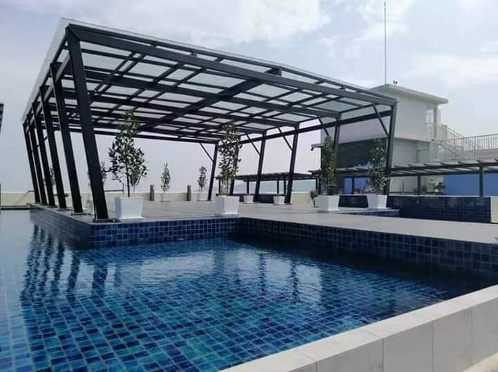 An open-air terrace features a swimming pool surrounded by a tiled deck. The structure has a modern design with a metal framework and glass roof, complemented by potted plants placed around the pool area.
