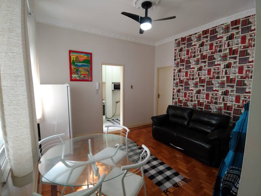 Sala ampla com TV à cabo, mesa, rede de casal, geladeira, ventilador de teto e sofá-cama