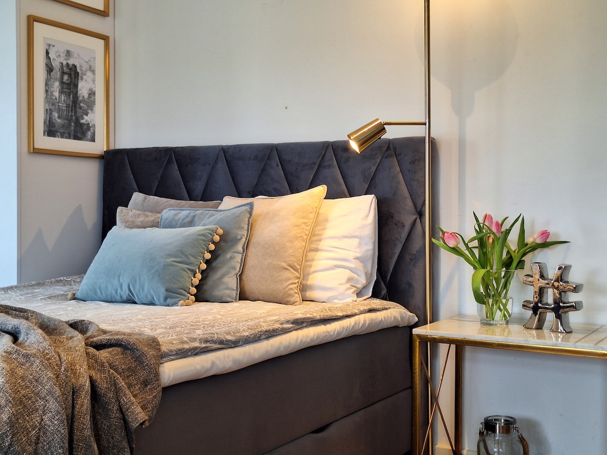 A cozy corner of the bedroom features a spacious bed adorned with plush pillows and a soft throw. A modern floor lamp provides warm light, while a small side table holds a vase of fresh flowers and decorative items, contributing to a sophisticated ambiance.