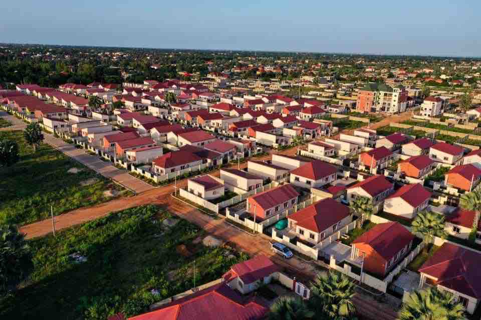 An aerial view captures a community of neatly arranged homes, each featuring red roofs. Green spaces and well-maintained roads line the neighborhood, while a variety of homes showcases a harmonious residential layout amidst the expansive landscape.