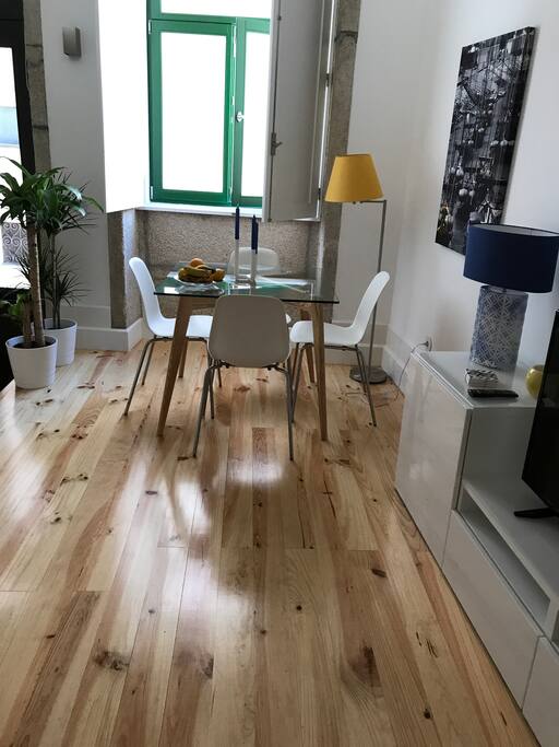 Zona comum com espaço de refeições, sofá cama, TV e kitchenette