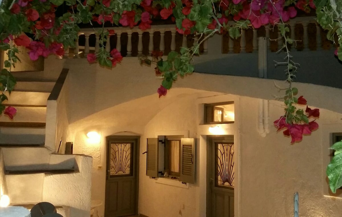 The entrance area features a softly lit staircase leading to the upper level, framed by vibrant pink bougainvillea. A series of doors with decorative glass inserts adds charm to the warm, whitewashed walls, enhancing the welcoming ambiance of the space.