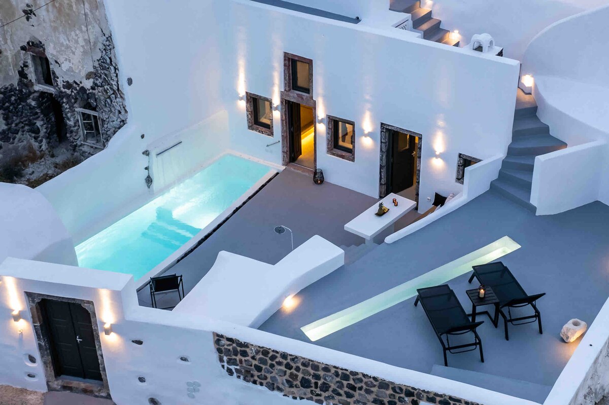 An aerial view of the outdoor pool area is presented, featuring a private swimming pool surrounded by a sleek gray terrace. Lounge chairs are positioned nearby for relaxation, with soft lighting illuminating the area for a serene ambiance during the evening.