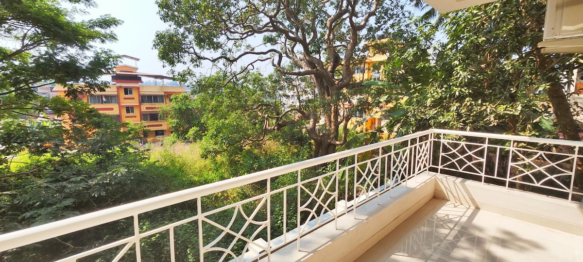 A private balcony offers a serene view of lush greenery, framed by trees. The railing features an elegant design, while the floor showcases a smooth surface, inviting relaxation in this tranquil outdoor space.
