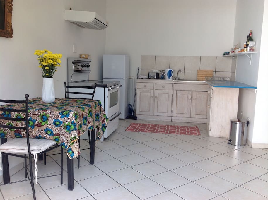 Open plan living area features full kitchen, small dining table, bookshelf and comfy sofa and armchair