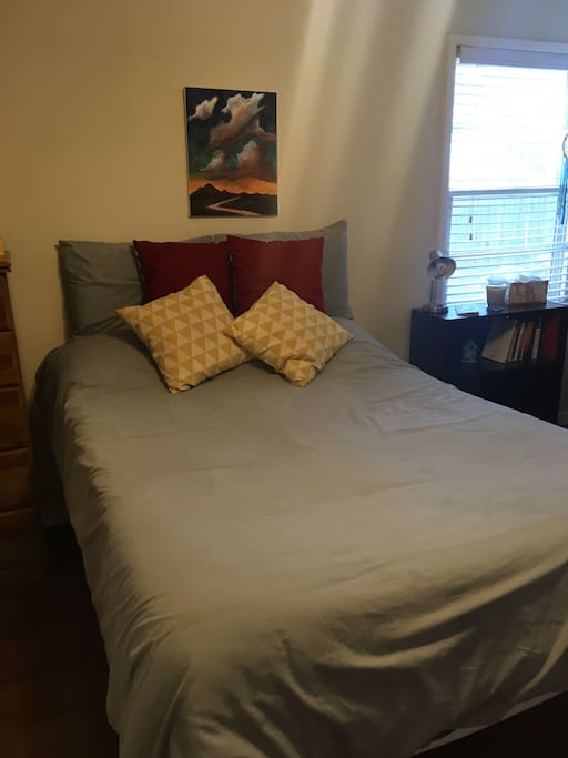 Full size bed, alongside a shelf of curated books of interest and a Lubbock guidebook.