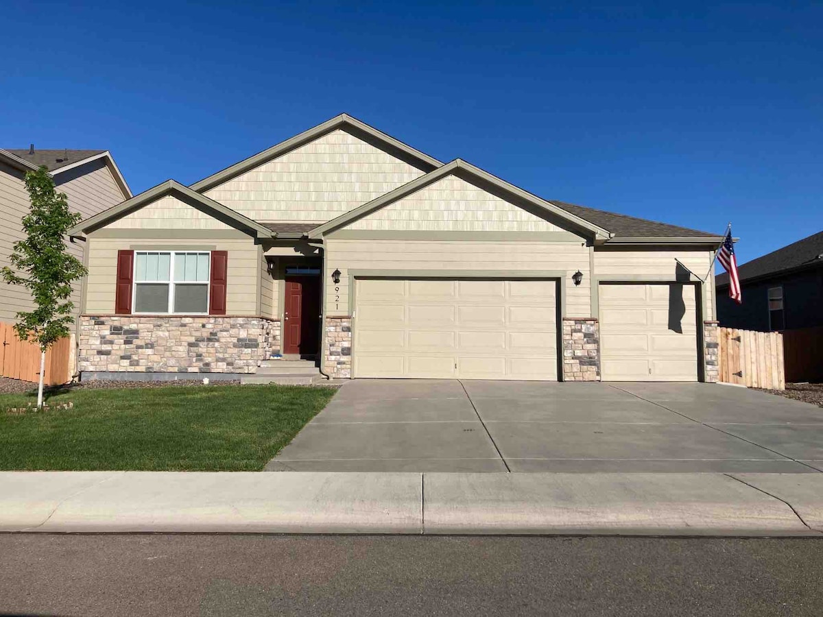 The exterior of the home is showcased, featuring a neutral colored facade with stone accents. A concrete driveway leads to a three-car garage. The front yard is well-maintained, with grass and a small tree. An American flag is displayed near the entrance.
