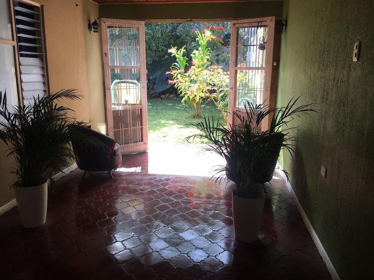 The entrance area features a tiled floor and potted plants on either side, creating a welcoming feel. Double doors open to a garden with lush greenery, allowing natural light to fill the space.