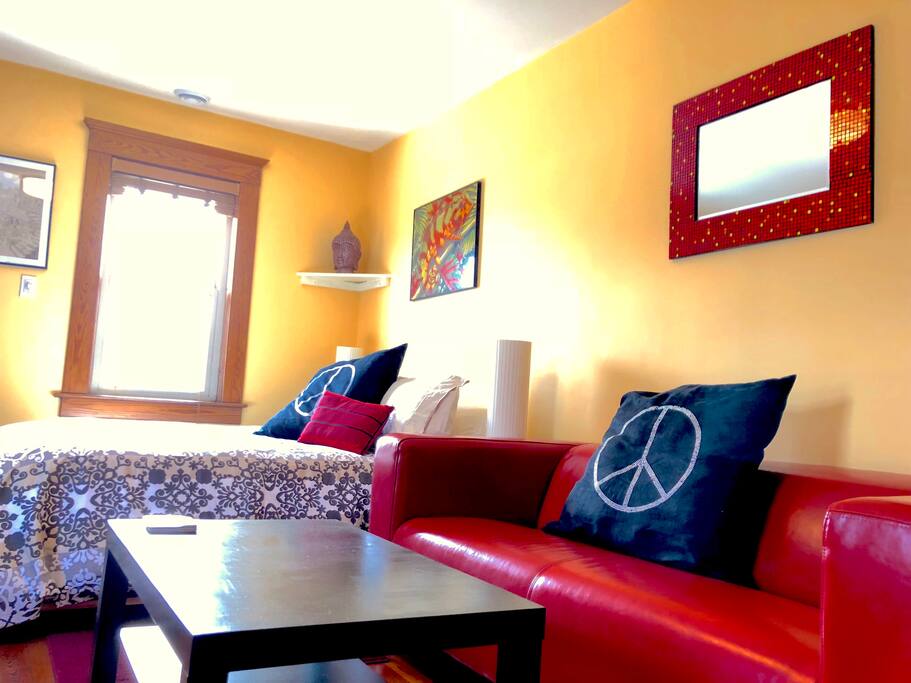 Sun-drenched master bedroom suite with original 1890s wooden floors, south- and east-facing windows, separate sitting area with sofa, coffee table, comfy reclining chairs, and 42" flatscreen HDTV
