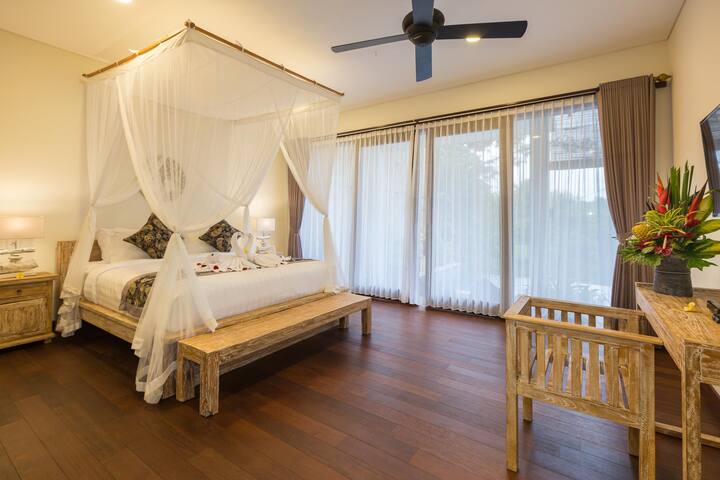 Airy bedroom with a four-poster bed draped in sheer white curtains, creating a dreamy and romantic space.  The room features hardwood floors and opens onto a balcony with scenic views.