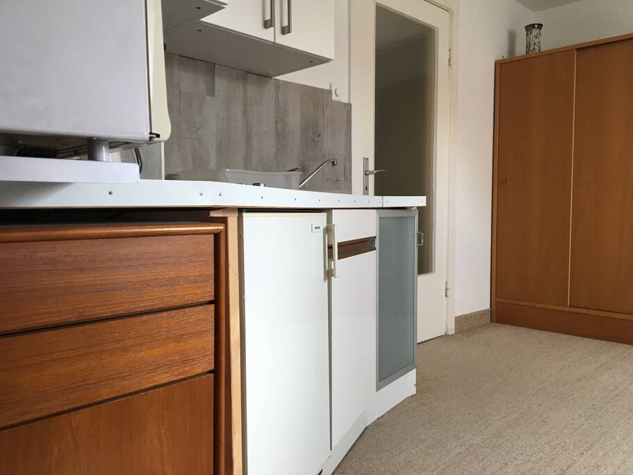 The kitchenette complete with refrigerator, oven and storage space.
Küchenzeile mit Hängeschränken, in denen sich das Geschirr befindet, Kühlschrank, Herd (zusätzlich zur Mikrowelle) und Stauraum für Putzmittel.