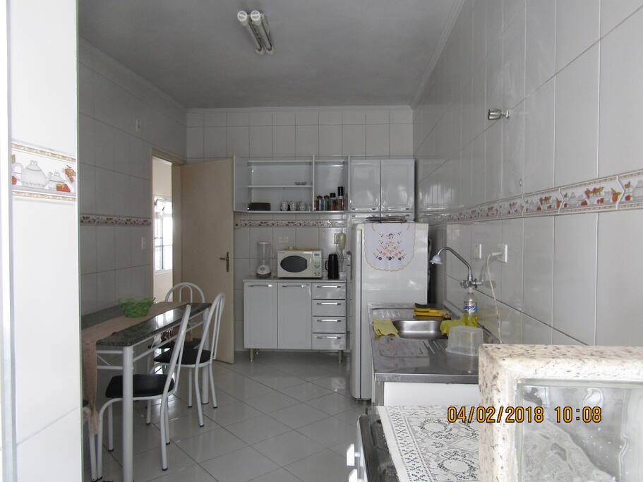 Cozinha com fogão,geladeira micro-ondas, liquidificador, pratos, copos, panelas e talheres.