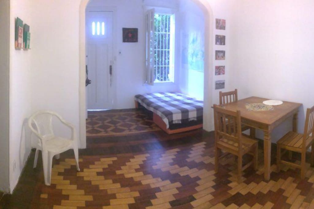 Sala de uso comum, com wifi, mesa de jantar, sofá-cama de casal e ventilador. Iluminada e arejada, com janelas amplas que dão para quintal externo e portas para ambos os quartos, corredor e cozinha.