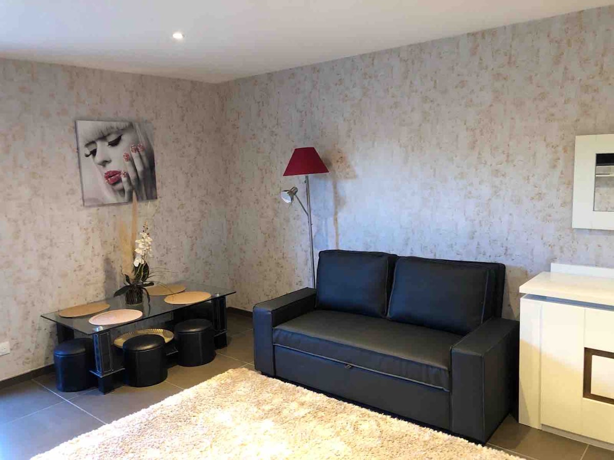 The living area features a dark sofa, paired with a low coffee table and sleek stools. A lamp stands in one corner, while a television is mounted on a light-colored wall. A soft area rug adds comfort to the space.