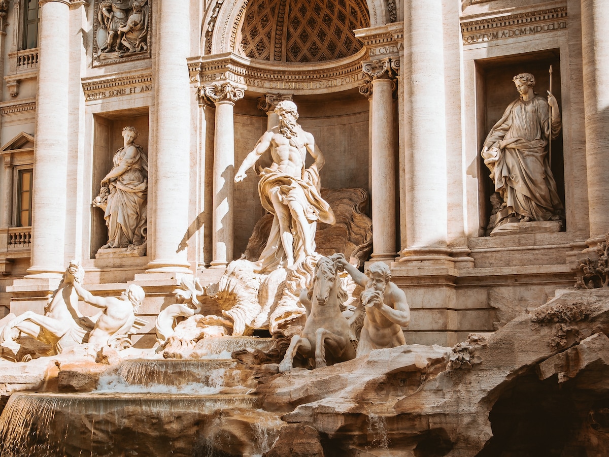 A grand fountain features intricately sculpted figures, including a prominent central statue wielding a trident. Surrounding elements include various mythical creatures and detailed architectural features, all crafted from stone. The fountain is enhanced by flowing water that adds a dynamic aspect to the scene.