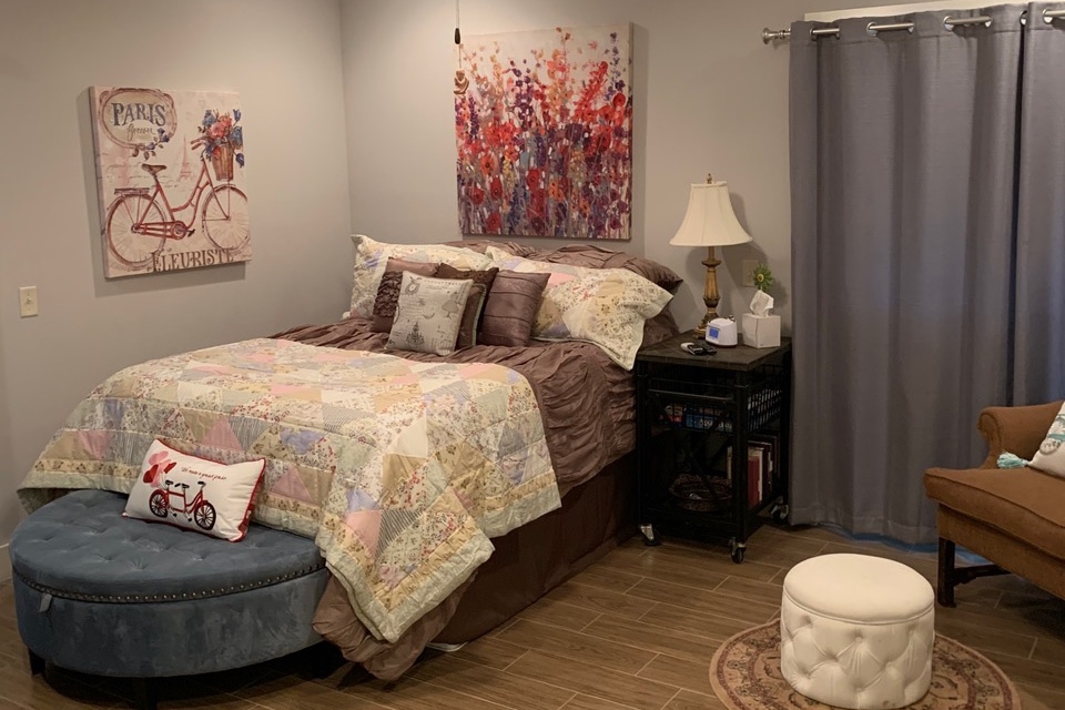 Dormitorio con cama tamaño queen con sábanas y almohadas, reloj despertador