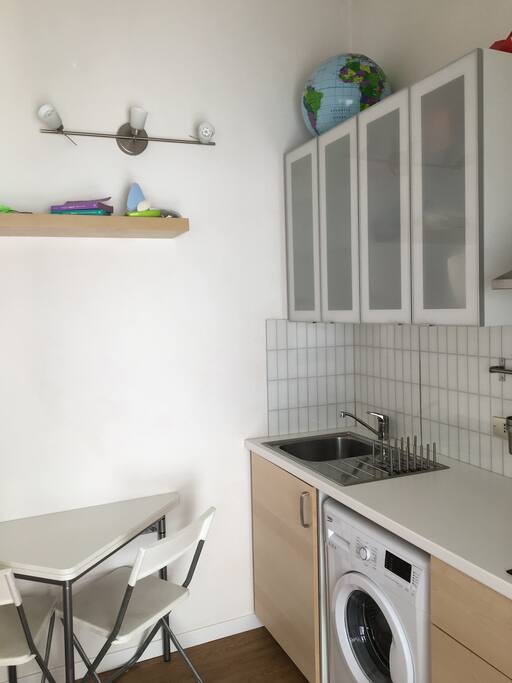 cucina con fornelli elettrici e lavatrice, due tavoli apribili con sei sedie pieghevoli