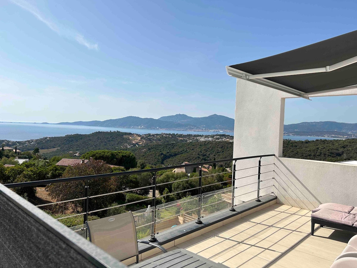 A spacious terrace is showcased, featuring a protective awning and a railing that overlooks a panoramic view of the gulf. The landscape includes rolling hills and the distant coastline, creating a serene backdrop for relaxation.
