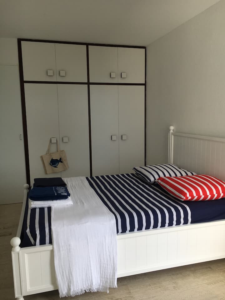 Habitación con un gran almacenamiento en toda una pared por medio armario y estantes y ventana con vistas al mar y ventilador