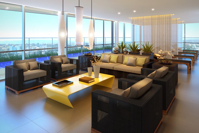 A modern communal lounge features large windows showcasing a scenic view. Comfortable black wicker seating is complemented by a yellow coffee table. Soft overhead lighting and green plants add a calming touch, creating a welcoming space for relaxation.